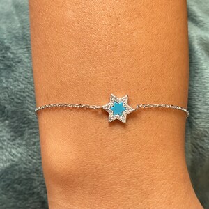 Könnte beinhalten: Ein silbernes Kettenarmband mit einem blauen Emaille-Davidstern-Anhänger. Der Stern ist von kleinen, klaren Steinen umgeben.