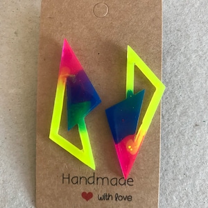 Puede incluir: Un par de pendientes de resina geom&eacute;tricos de color amarillo ne&oacute;n y arco&iacute;ris. Los pendientes se muestran en una tarjeta marr&oacute;n con el texto "Handmade with love".