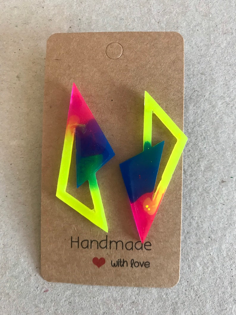 Puede incluir: Un par de pendientes de resina geom&eacute;tricos de color amarillo ne&oacute;n y arco&iacute;ris. Los pendientes se muestran en una tarjeta marr&oacute;n con el texto "Handmade with love".