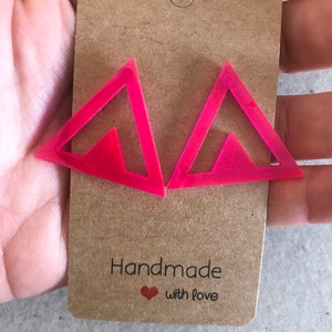 May include: A pair of pink triangle shaped earrings with a smaller triangle cutout inside. The earrings are handmade with love.