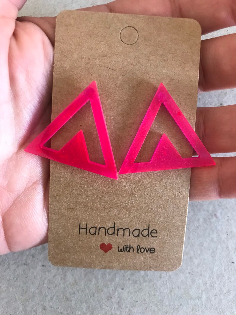 May include: A pair of pink triangle shaped earrings with a smaller triangle cutout inside. The earrings are handmade with love.