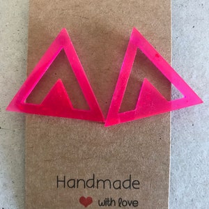 May include: A pair of pink triangle shaped earrings with a cutout design. The earrings are on a brown card with the text "Handmade with love".