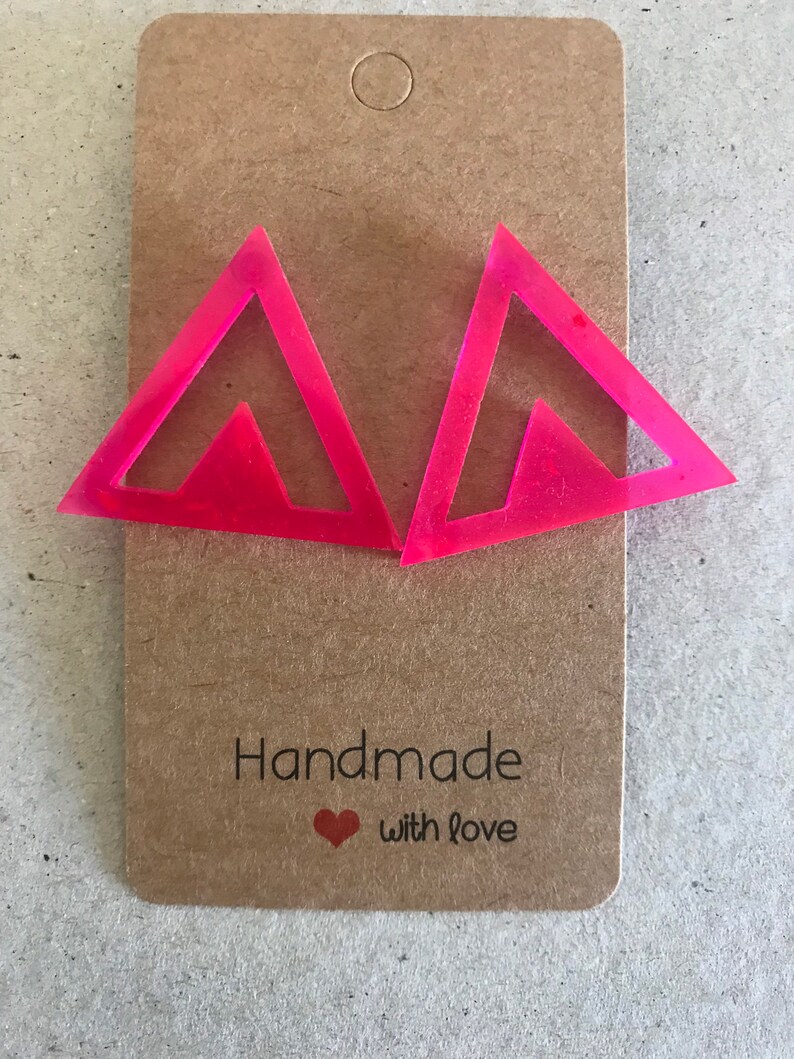 May include: A pair of pink triangle shaped earrings with a smaller triangle cut out in the center. The earrings are handmade with love.
