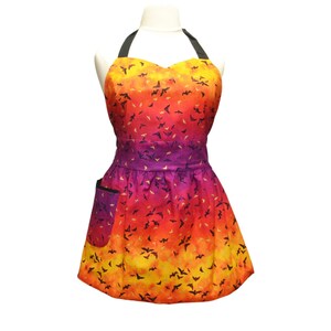 May include: A purple, orange, and yellow apron with a black halter strap and a black pocket. The apron is covered in a pattern of black bats.