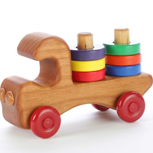 May include: A wooden toy truck with a stackable ring toy on the back. The truck is brown and has red wheels. The rings are purple, yellow, red, blue, and green.