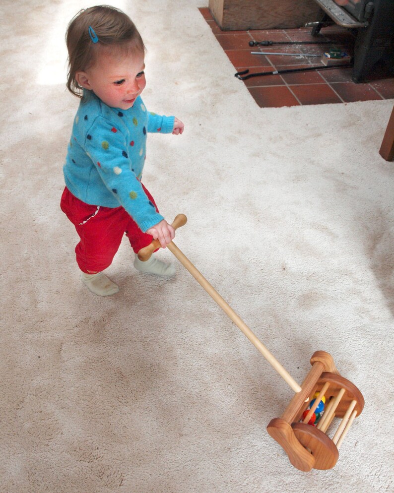 Handmade wooden lawnmower push toy for toddlers. Toddlers can also move the toy back and forth to pretend to vacuum. Sturdy construction includes a beautiful wood turned handle easily grasped with two hands to aid in learning to walk.