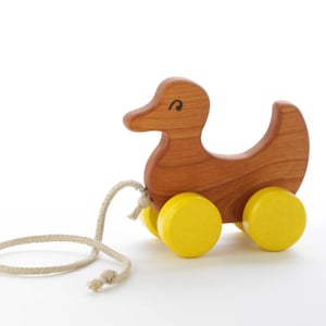 May include: A wooden toy duck with yellow wheels and a pull string. The duck is brown and has a simple painted eye.