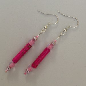 May include: A pair of pink and silver earrings with a long, cylindrical pink bead and smaller pink beads. The earrings have silver hooks.