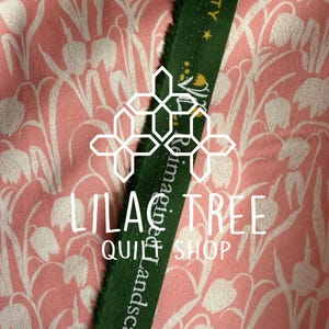 May include: Pink fabric with a white floral pattern and a green ribbon. The ribbon has white text that reads "Reimagined Landscapes Society". The text "LILAC TREE QUILT SHOP" is also visible.