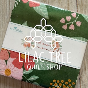 May include: A stack of fabric squares in a clear plastic wrapper. The fabric has a green background with a floral pattern in pink, yellow, and white. The label reads "Meadow Moments" and "Lilac Tree Quilt Shop."