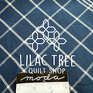 May include: Navy blue fabric with a white plaid pattern. The text "LILAC TREE QUILT SHOP moda" is visible, along with "Summer Solstice 18" wide Towelings". A white geometric design is also present.