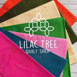 May include: A stack of eight fabric squares with a splatter pattern in various colors, including orange, green, beige, teal, pink, and lime green. The fabric squares are arranged in a fan shape and have a white text overlay that reads "Lilac Tree Quilt Shop".