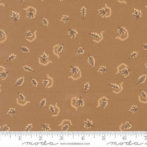 May include: A tan fabric featuring a repeating pattern of small dark brown leaves and light beige sprigs. A white ruler is visible at the bottom edge, showing measurements in inches, with the text moda and www.modafabrics.com printed on it.