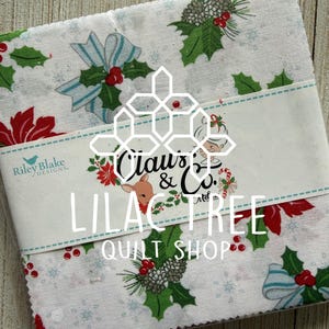 May include: A stack of Christmas-themed fabric squares in a clear plastic package. The fabric features a white background with holly, pinecones, red berries, and blue bows. The text "Claus & Co." and "Lilac Tree Quilt Shop" is visible.