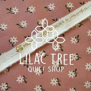 May include: Pink fabric with a white daisy floral pattern and a white trim. The trim has gold text that reads "IMAGINA FLOWER BY SINGIBER © moda". The text "LILAC TREE QUILT SHOP" is also visible.