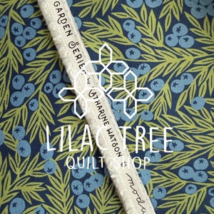 May include: Close-up of fabric with a blue and green floral pattern featuring blueberries and leaves. A white ribbon with the text "GARDEN SERIES by KATHARINE WATSON" and "LILAC TREE QUILT SHOP" is visible. The fabric is from moda FABRICS.