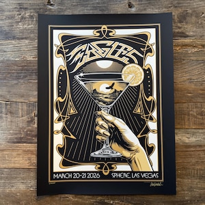 May include: A black and gold concert poster for the Eagles, featuring a martini glass with a sunset scene. The poster includes the text "EAGLES" at the top, and "MARCH 20-21 2026 SPHERE LAS VEGAS" at the bottom.
