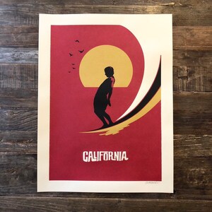 Pu&ograve; includere: Un poster rosso e oro con la silhouette di una persona che fa surf su un'onda. Il sole sta tramontando sullo sfondo e ci sono uccelli che volano nel cielo. Il testo "CALIFORNIA" &egrave; stampato nella parte inferiore del poster.