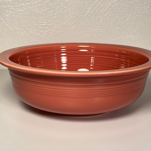 May include: A coral-colored ceramic bowl with a wide rim and a smooth, glossy finish. The bowl has a slightly rounded shape and is perfect for serving salads, snacks, or desserts.