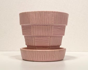 May include: A pink ceramic planter with a ribbed design and a matching saucer. The planter has a square shape with rounded corners and a wide base.