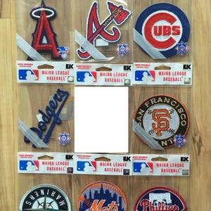 May include: Nine embroidered iron-on patches featuring Major League Baseball team logos. The logos are for the Atlanta Braves, Chicago Cubs, Los Angeles Dodgers, San Francisco Giants, Seattle Mariners, New York Mets, Philadelphia Phillies, and two others. The patches are packaged in clear plastic.