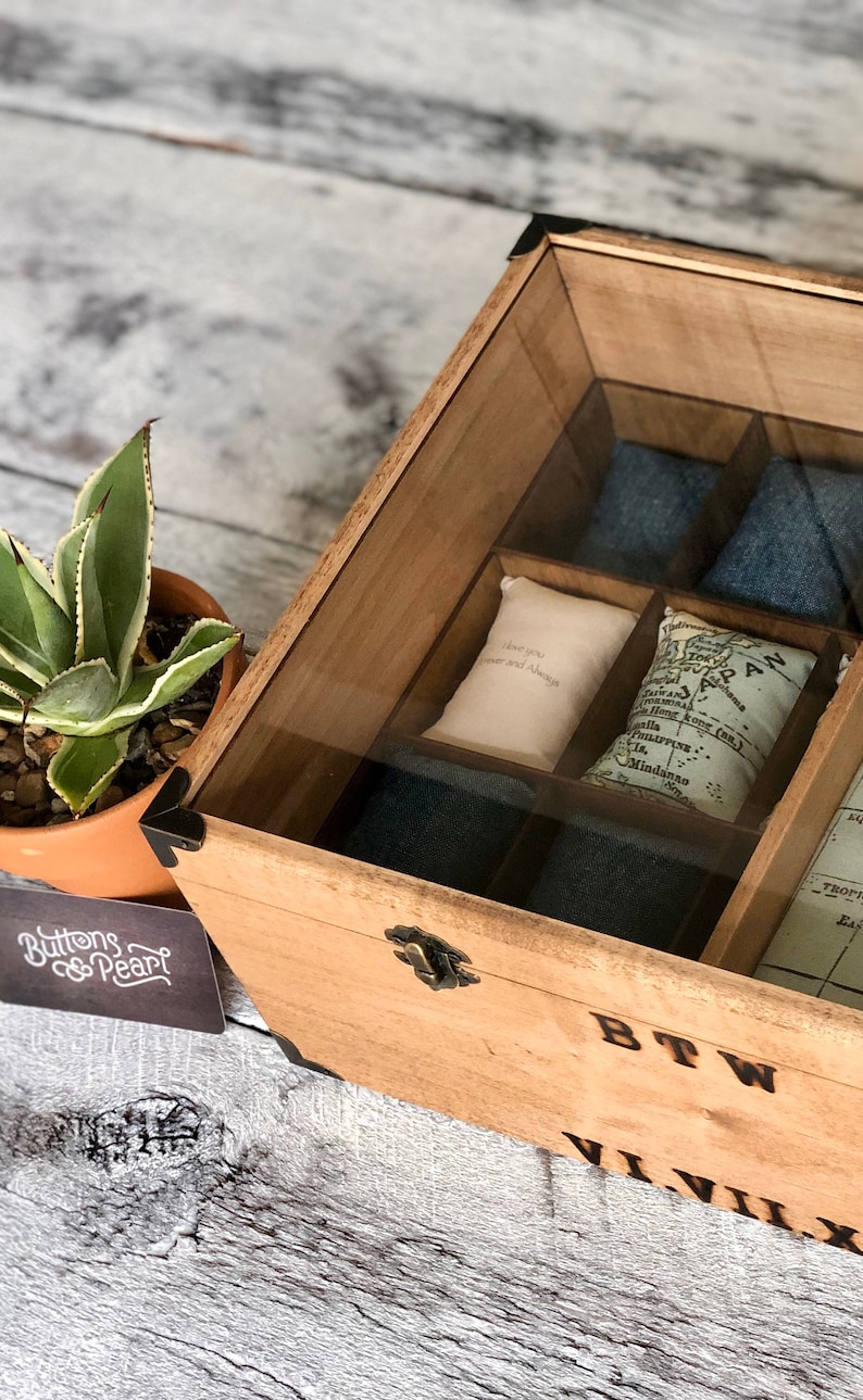 Puede incluir: Una caja de madera con tapa de vidrio, dividida en compartimentos. La caja contiene peque&ntilde;as bolsas de tela con las palabras "Te amo para siempre y siempre" y un mapa de Jap&oacute;n. La caja tiene las palabras "BTW" y "VIVIX" grabadas en la parte delantera.