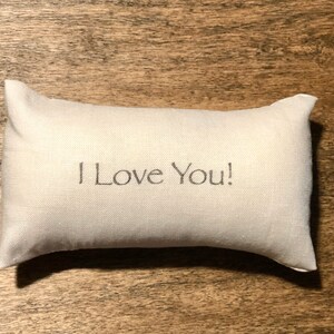 Puede incluir: Una almohada blanca con el texto "I Love You!" bordado.