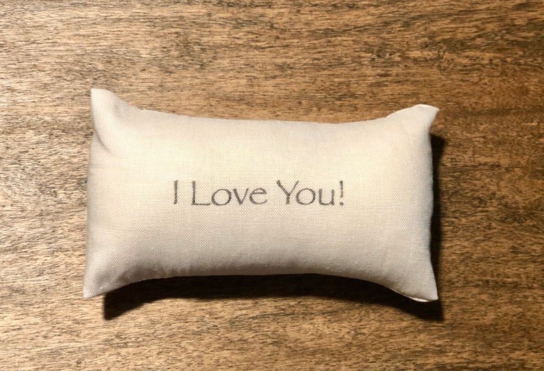 Puede incluir: Una almohada blanca con el texto "I Love You!" bordado.