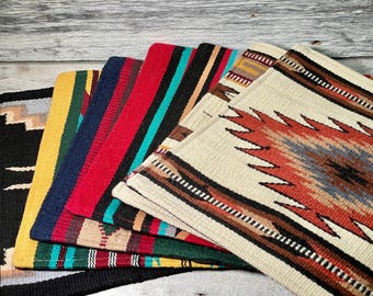 May include: A stack of five colorful woven rugs with geometric patterns. The rugs are made of wool and have a variety of colors, including red, blue, yellow, and brown.