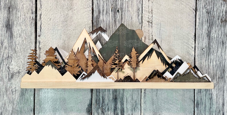 May include: A wooden mountain range wall decor with a layered design. The mountains are painted in shades of brown, black, and white. The piece is mounted on a wooden shelf.