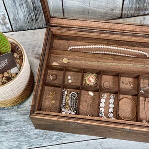 May include: A wooden jewelry box with a glass lid, divided into compartments, filled with various jewelry pieces, including necklaces, earrings, bracelets, and rings. The box is labeled "Buttons & Pearl".