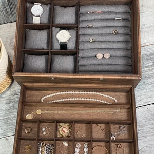 May include: A wooden jewelry box with a glass top and a drawer. The top compartment has compartments for watches, rings, and earrings. The drawer has compartments for necklaces, bracelets, and other jewelry.