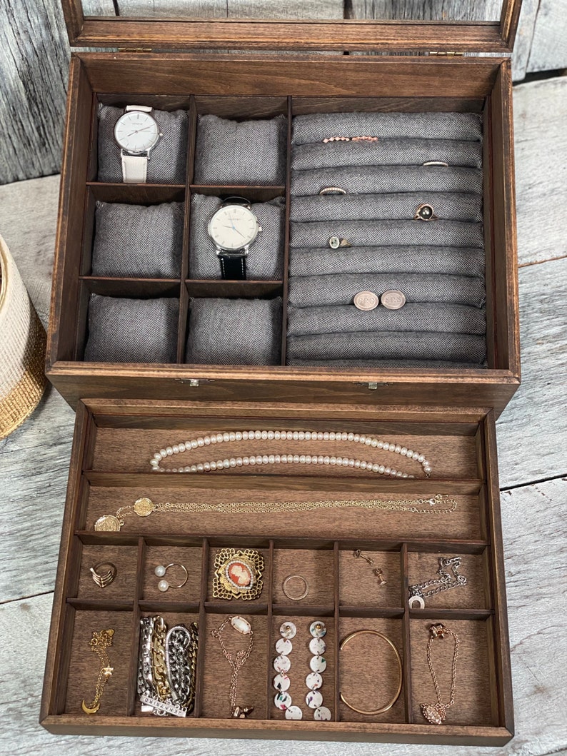 May include: A wooden jewelry box with a glass top and a drawer. The top compartment has compartments for watches, rings, and earrings. The drawer has compartments for necklaces, bracelets, and other jewelry.