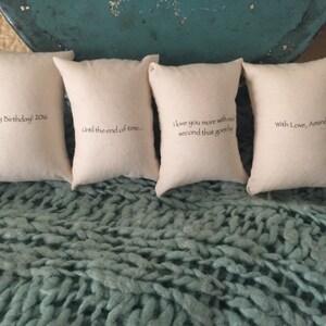 Puede incluir: Cuatro peque&ntilde;as fundas de almohada blancas con diferentes mensajes bordados. Los mensajes son "Happy Birthday! 2016", "Until the end of time.", "I love you more with each second that goes by" y "With Love, Amanda".