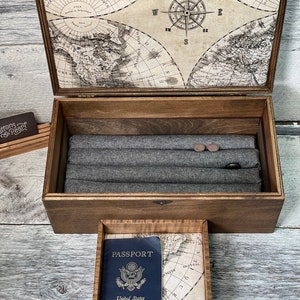 May include: A wooden box with a compass design on the lid. The box is open and contains a grey fabric lining and a small wooden box with a passport inside. The passport is blue and has the words "United States of America" printed on it.