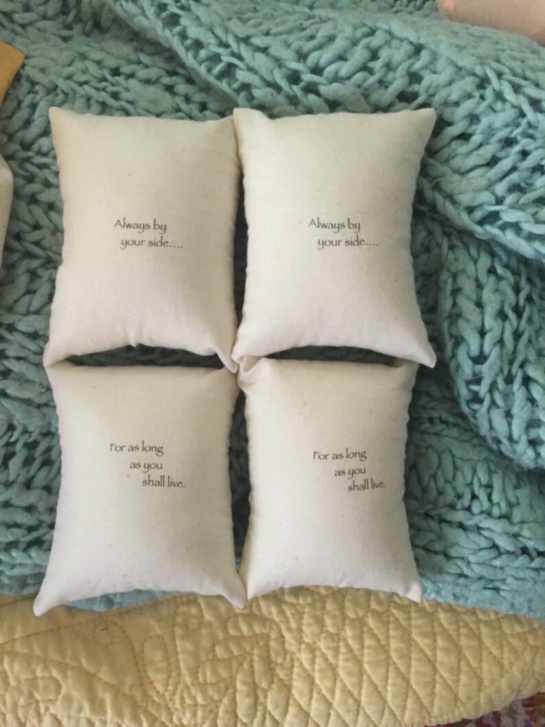 Puede incluir: Cuatro peque&ntilde;os cojines de tela blanca con texto bordado. Los cojines tienen el texto "Always by your side..." y "For as long as you shall live." Los cojines est&aacute;n dispuestos en dos filas de dos sobre una superficie azul claro y amarilla.