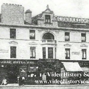 May include: A black and white photo of a building with the text "Cumbrae Hotel Bar" above the entrance. The building has a large arched window and several smaller windows. There are people walking in front of the building.