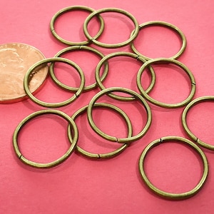May include: A pile of 10 antique gold jump rings, approximately 1 inch in diameter, on a pink surface.