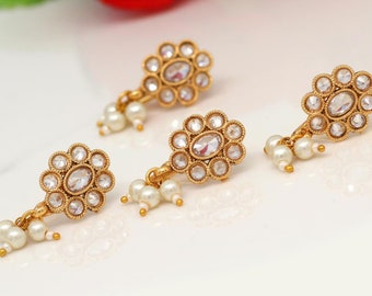 May include: Close-up of four gold-toned nose rings. Each ring features a central oval-shaped clear stone surrounded by smaller clear stones, with a floral design. Small white pearls dangle from each ring. The text "THE NOSE RING QUEEN ON ETSY" is at the bottom.