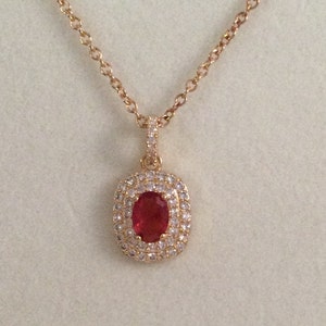 Puede incluir: Un collar de cadena de oro con un colgante que presenta una gran piedra ovalada roja rodeada de piedras pequeñas transparentes.