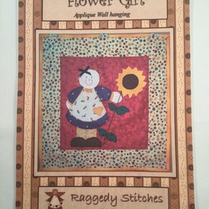 May include: A pattern for an appliqué wall hanging featuring a flower girl holding a sunflower. The pattern is titled "Flower Girl" and is by "Raggedy Stitches by Michelle Pearson".