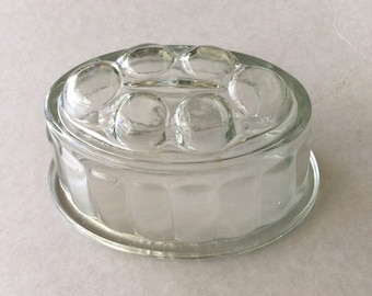 May include: A clear glass mold with a fluted base and a domed top with a pattern of raised circles. The mold is designed for making desserts like jellies or puddings.