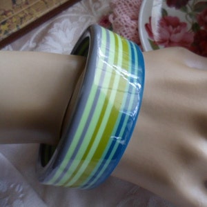 May include: A wide, colorful bangle bracelet with stripes of teal, green, yellow, and gray.