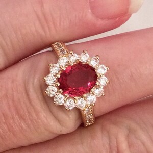 May include: A gold ring with a large oval red gemstone surrounded by smaller clear gemstones.