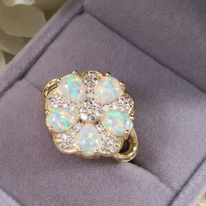 Puede incluir: Un anillo de oro con un diseño de flor con cinco ópalos blancos y pequeñas piedras transparentes.