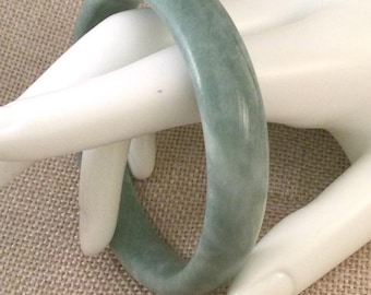 May include: A pale green jade bangle bracelet. The bangle is smooth and polished.