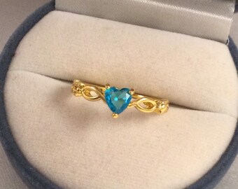 May include: A gold ring with a delicate, intertwined design features a heart-shaped blue gemstone.