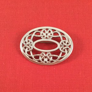 Puede incluir: Un broche ovalado de plata con un diseño de nudo celta.