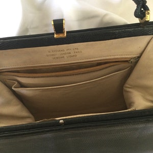 Può includere: Borsa a mano in pelle nera con chiusura dorata e tasca con zip. L'interno della borsa è foderato in tessuto beige. La borsa ha un'etichetta che recita "H.S. Stevens Pty. Ltd. Sydney, Londra, Parigi Genuine Lizard."