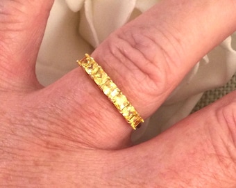 May include: A gold band ring with a row of small, square-shaped, yellow gemstones.